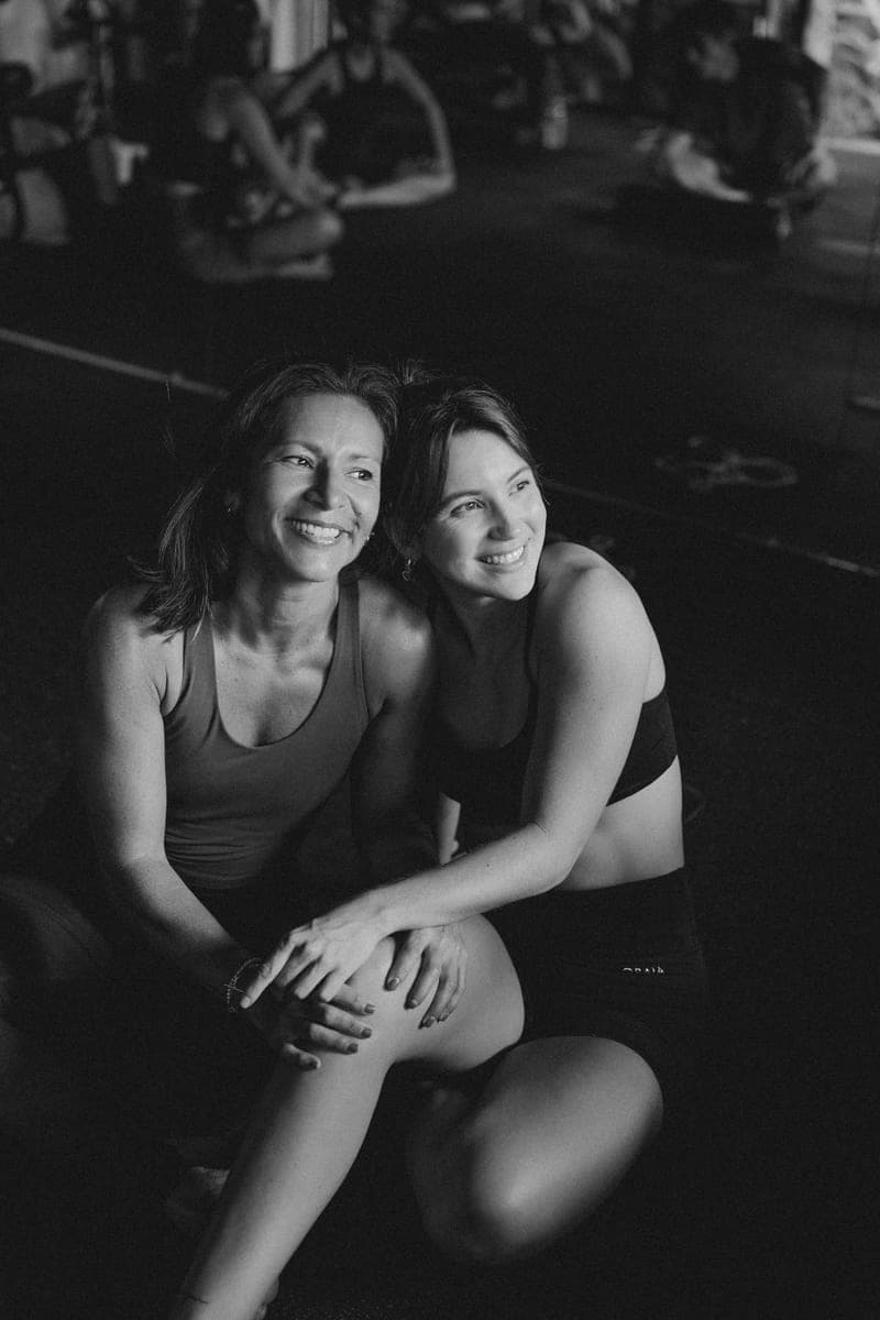 Black-and-white photo of two women sitting side by side in the studio, smiling.