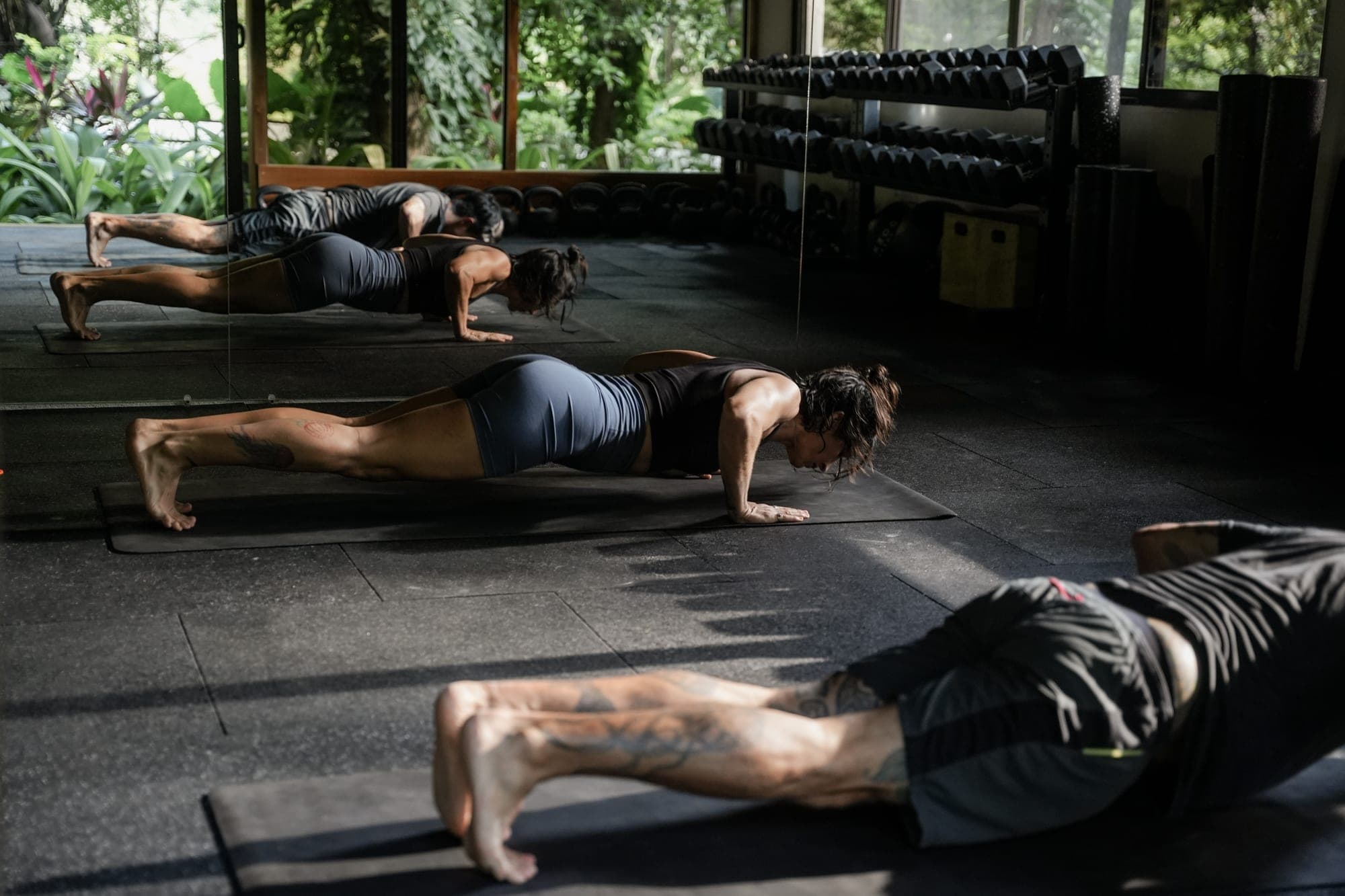 Inside the open-walled studio, people hold plank positions on their mats, with racks of dumbbells and the jungle beyond.